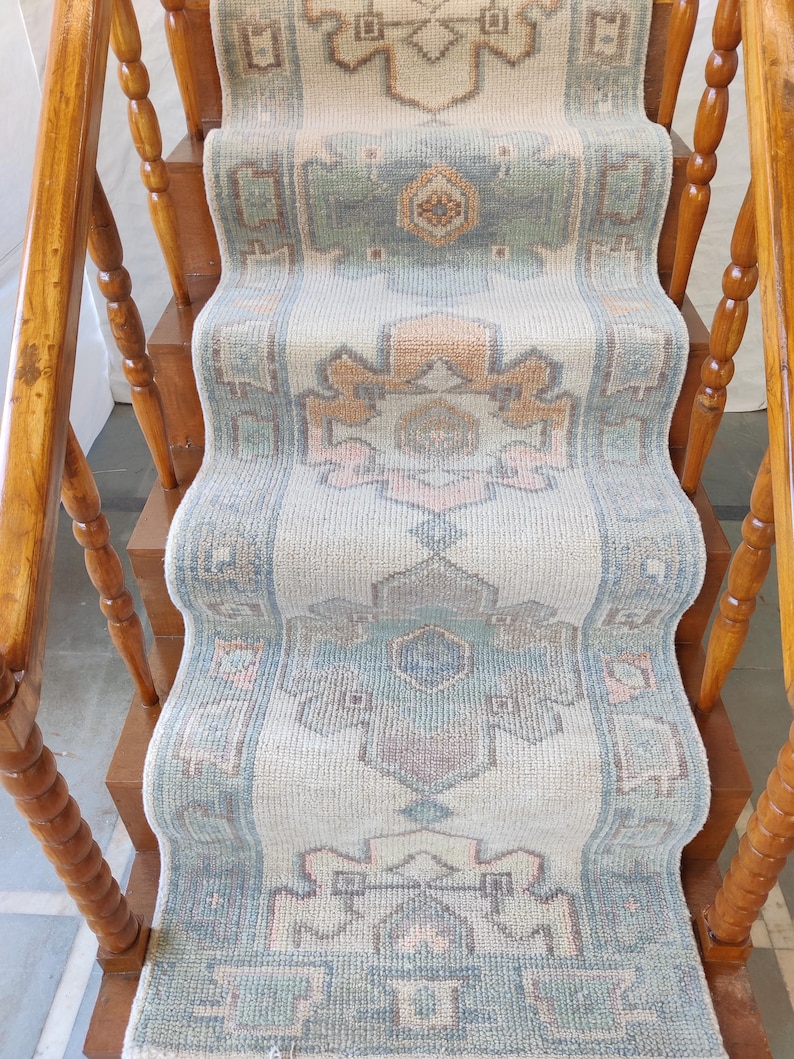May include: A light blue and beige patterned rug runner with a geometric design. The rug is on a wooden staircase with a wooden handrail.