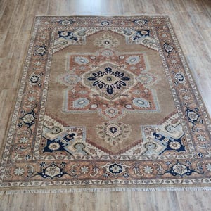 May include: A traditional Persian rug with a beige background and intricate floral patterns in shades of blue, red, and brown. The rug has a fringed border and a central medallion.
