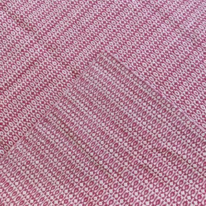 May include: A close-up of a woven textile with a repeating diamond pattern. The fabric is primarily a deep red color with a contrasting off-white pattern. The texture appears soft and the weave is tight.