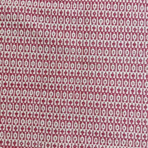 May include: Close-up of a woven textile with a repeating pattern. The design features a series of small, white, diamond-shaped motifs set against a red background. The fabric has a textured appearance, suggesting a natural fiber.