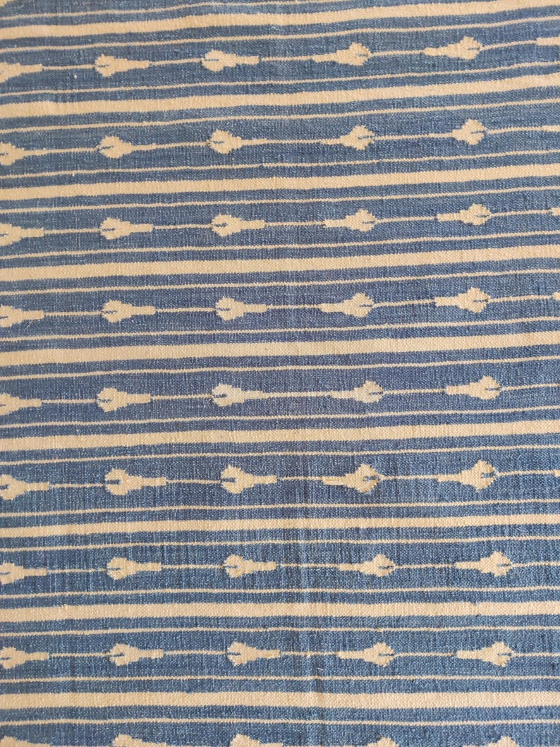 Op de afbeelding: Een close-up van een blauw-wit gestreepte stof met een herhalend patroon van kleine witte druppelvormen.