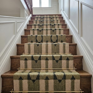 May include: A staircase featuring a woven runner with a geometric pattern in olive green, dark charcoal, and beige. The runner is secured to the wooden steps with polished brass stair rods that span the width of the carpeted section.