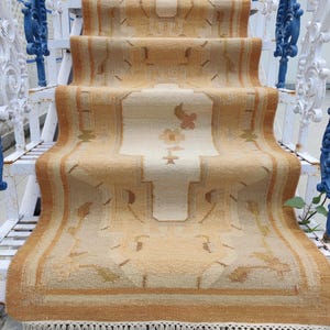 May include: A beige and brown patterned rug with fringe on the bottom edge. The rug is laid out on a set of white stairs with a blue metal railing.