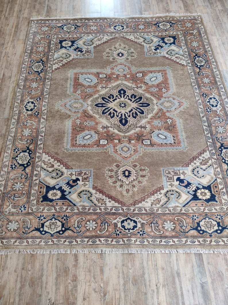 May include: A brown rug with a beige and blue patterned design. The rug has a fringe border.