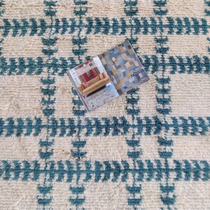May include: A white and teal blue patterned rug with a magazine on top of it. The magazine has a colorful abstract design on the cover.