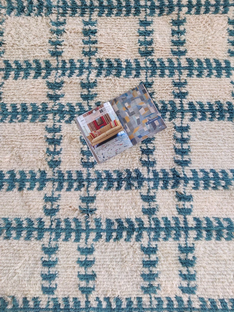 May include: A white and teal blue patterned rug with a magazine on top of it. The magazine has a colorful abstract design on the cover.