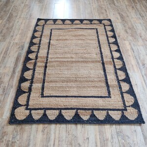 May include: A natural fiber rug with a black and tan border and a pattern of black teardrop shapes around the edge.