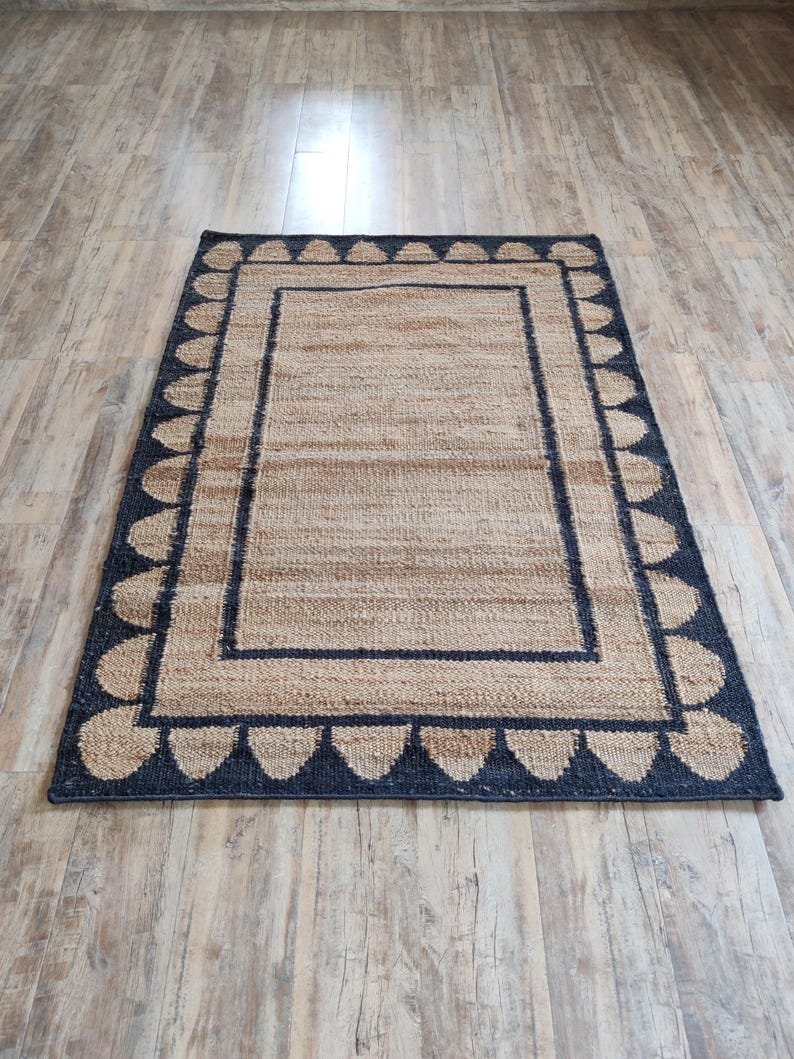 May include: A natural fiber rug with a black and tan border and a pattern of black teardrop shapes around the edge.