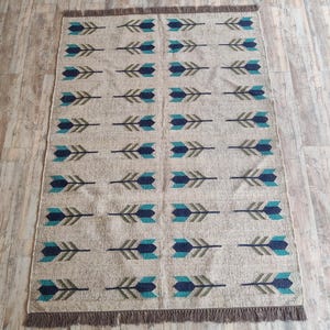 May include: A beige rug with a repeating pattern of blue and green arrows. The rug has a fringe border.