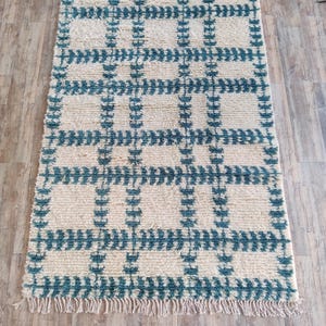 May include: A white and teal rug with a geometric pattern. The rug has a fringe border.