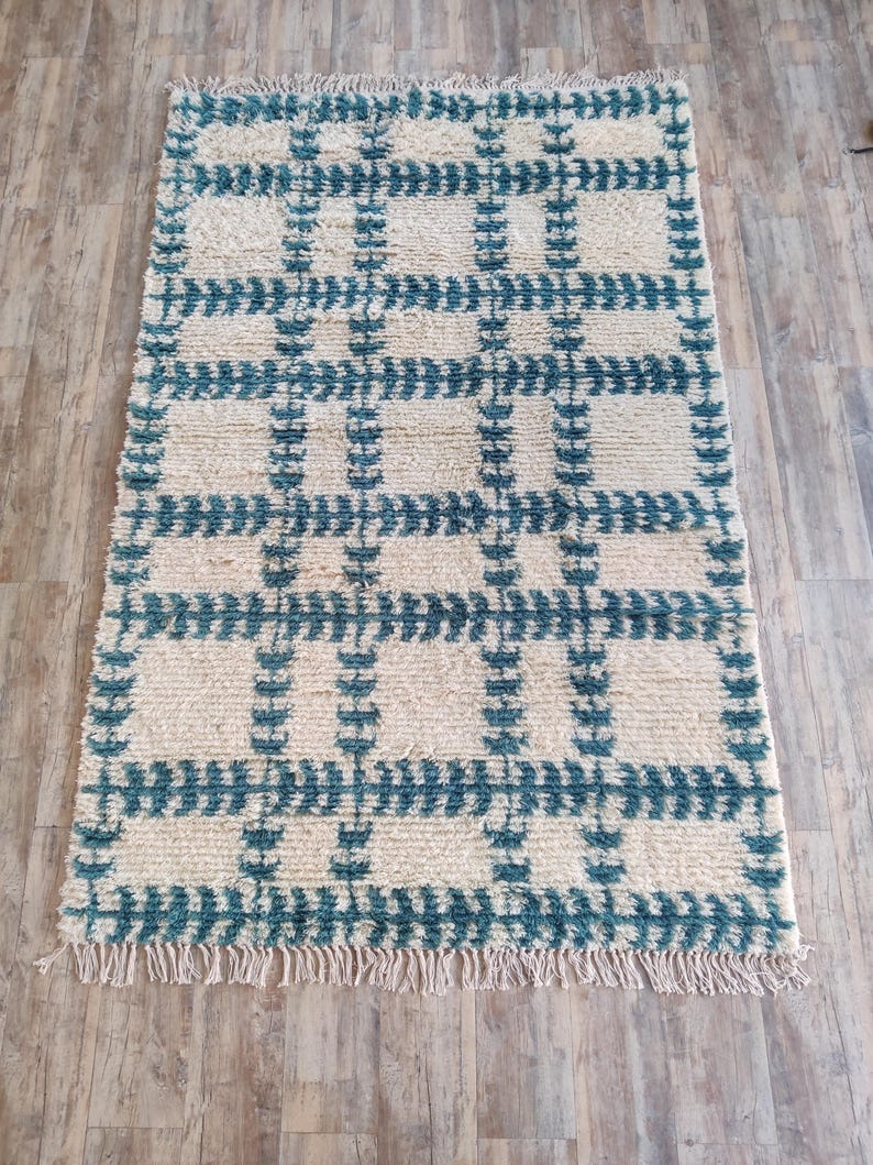 May include: A white and teal rug with a geometric pattern. The rug has a fringe border.