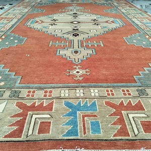 Op de afbeelding: Een vintage tapijt met een traditioneel geometrisch patroon in tinten rood, blauw en beige. Het tapijt heeft een centraal medaillon met een herhalend ontwerp van ruiten en vierkanten.