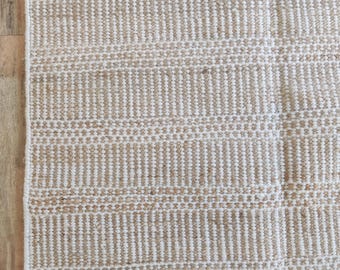 May include: A white and beige striped rug with a woven texture. The rug has a subtle sheen and a slightly rough surface.