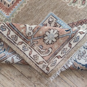 May include: A close-up of a beige and brown patterned rug with a fringe border. The rug is folded in half, showing the intricate details of the design.
