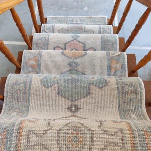 May include: A set of four beige and white patterned rugs with a geometric design. The rugs are layered on a wooden staircase.