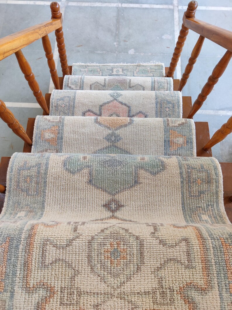 May include: A set of four beige and white patterned rugs with a geometric design. The rugs are layered on a wooden staircase.