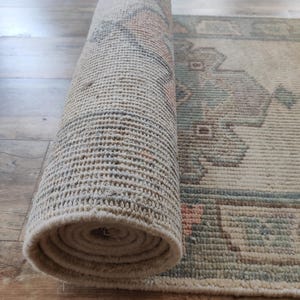 May include: A rolled up beige rug with a geometric pattern in shades of blue, green, and pink. The rug is woven with a textured surface.