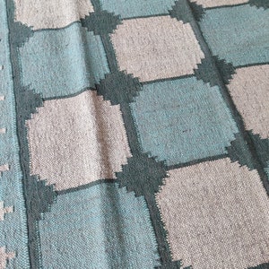 May include: A woven rug with a checkered pattern in shades of teal, gray, and dark green.