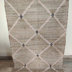 May include: A beige and pink handwoven rug with a diamond pattern and black accents. The rug has a fringe border.