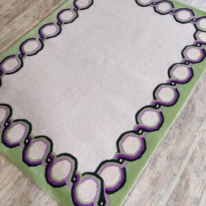 Hand tufted wool rug with green border and purple chain pattern on neutral background, modern designer area rug for living room or bedroom