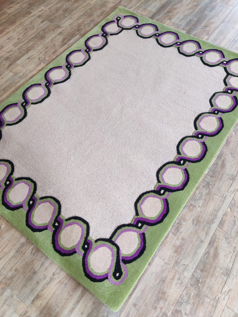 Hand tufted wool rug with green border and purple chain pattern on neutral background, modern designer area rug for living room or bedroom