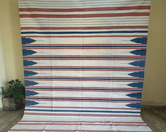 May include: A white, blue, and red striped throw blanket with a geometric pattern. The blanket has a fringe border.