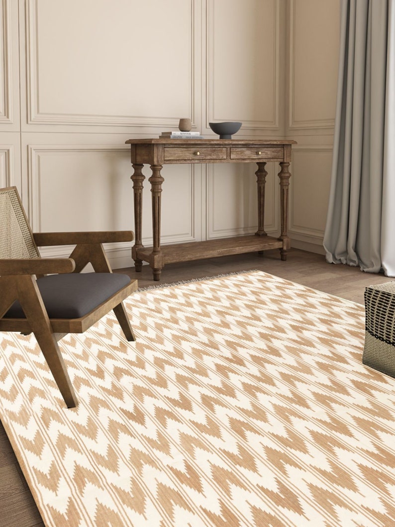 Puede incluir: Una alfombra con estampado blanco y marr&oacute;n con dise&ntilde;o de chevron. La alfombra est&aacute; en un sal&oacute;n con una consola de madera y una silla.