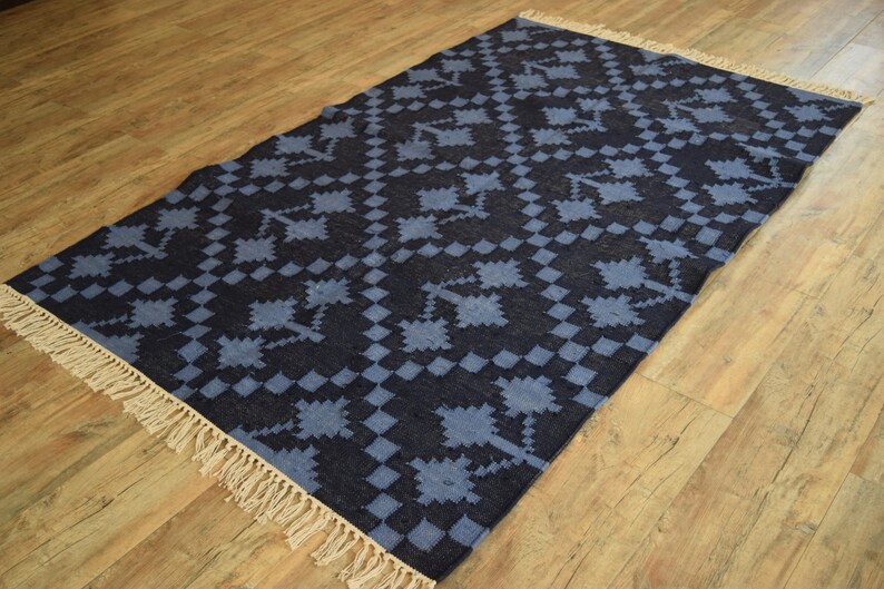 Puede incluir: Una alfombra azul y negra con estampado y borde de flecos. La alfombra tiene un dise&ntilde;o geom&eacute;trico con un patr&oacute;n de cuadros.