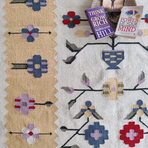 handwoven wool rug features a floral tribal kilim design with soft beige, red, blue, and pastel tones. Made from premium natural wool, this flatweave rug is durable, eco-friendly, and perfect for living rooms, bedrooms, or boho home décor. Each rug is handcrafted by skilled artisans, making it a unique and timeless piece for modern and traditional interiors.