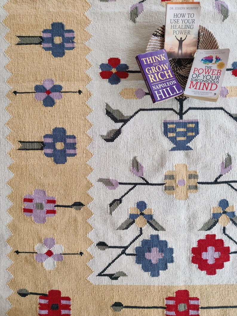 handwoven wool rug features a floral tribal kilim design with soft beige, red, blue, and pastel tones. Made from premium natural wool, this flatweave rug is durable, eco-friendly, and perfect for living rooms, bedrooms, or boho home décor. Each rug is handcrafted by skilled artisans, making it a unique and timeless piece for modern and traditional interiors.