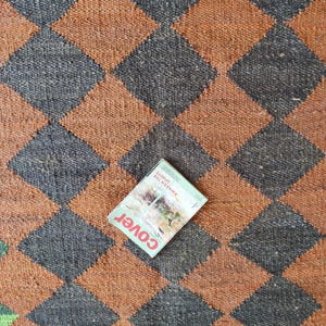 K&ouml;nnte beinhalten: Ein brauner und schwarzer Schachbrettteppich mit einem Magazin darauf. Das Magazincover hat das Wort "Cover" und den Text "Awaken the Spirits" in Wei&szlig;.