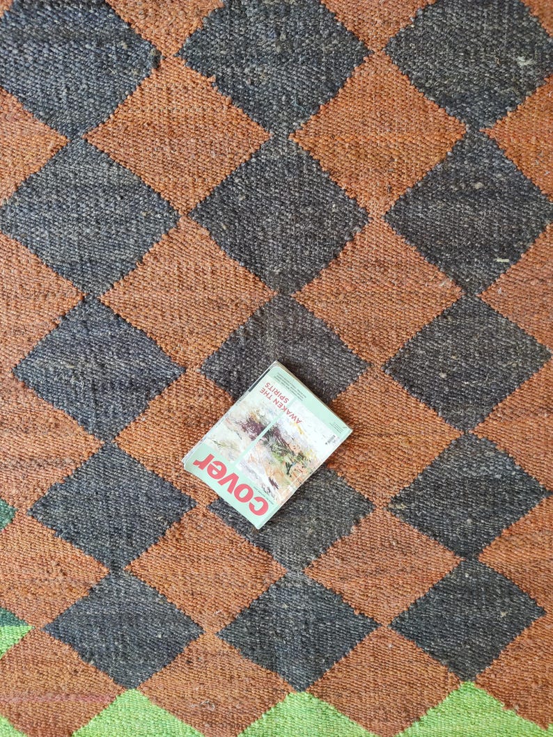 K&ouml;nnte beinhalten: Ein brauner und schwarzer Schachbrettteppich mit einem Magazin darauf. Das Magazincover hat das Wort "Cover" und den Text "Awaken the Spirits" in Wei&szlig;.