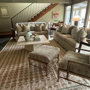 May include: A living room featuring a large area rug, two sofas, a coffee table, an ottoman, and a chair. The rug is a light brown with a geometric pattern. The sofas are beige with light brown cushions. The coffee table is white with a marble top. The ottoman is beige with a brown pattern. The chair is beige with a brown pattern.