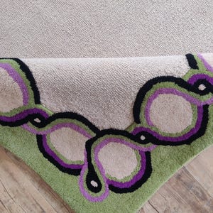 Hand tufted wool rug with green border and purple chain pattern on neutral background, modern designer area rug for living room or bedroom