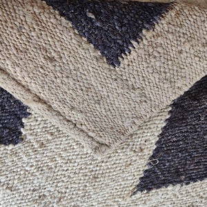 K&ouml;nnte beinhalten: Nahaufnahme eines Naturfaser-Teppichs mit geometrischem Muster. Der Teppich ist aus Jute und hat eine schwarze und nat&uuml;rliche Farbgebung.
