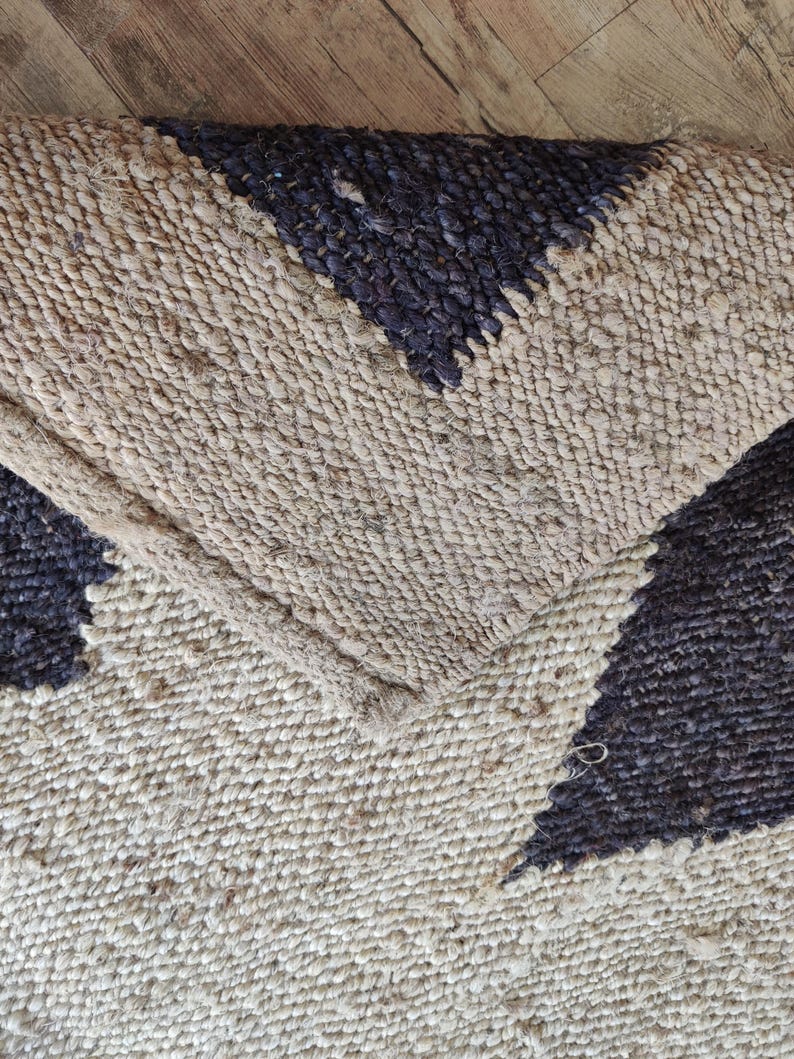 K&ouml;nnte beinhalten: Nahaufnahme eines Naturfaser-Teppichs mit geometrischem Muster. Der Teppich ist aus Jute und hat eine schwarze und nat&uuml;rliche Farbgebung.