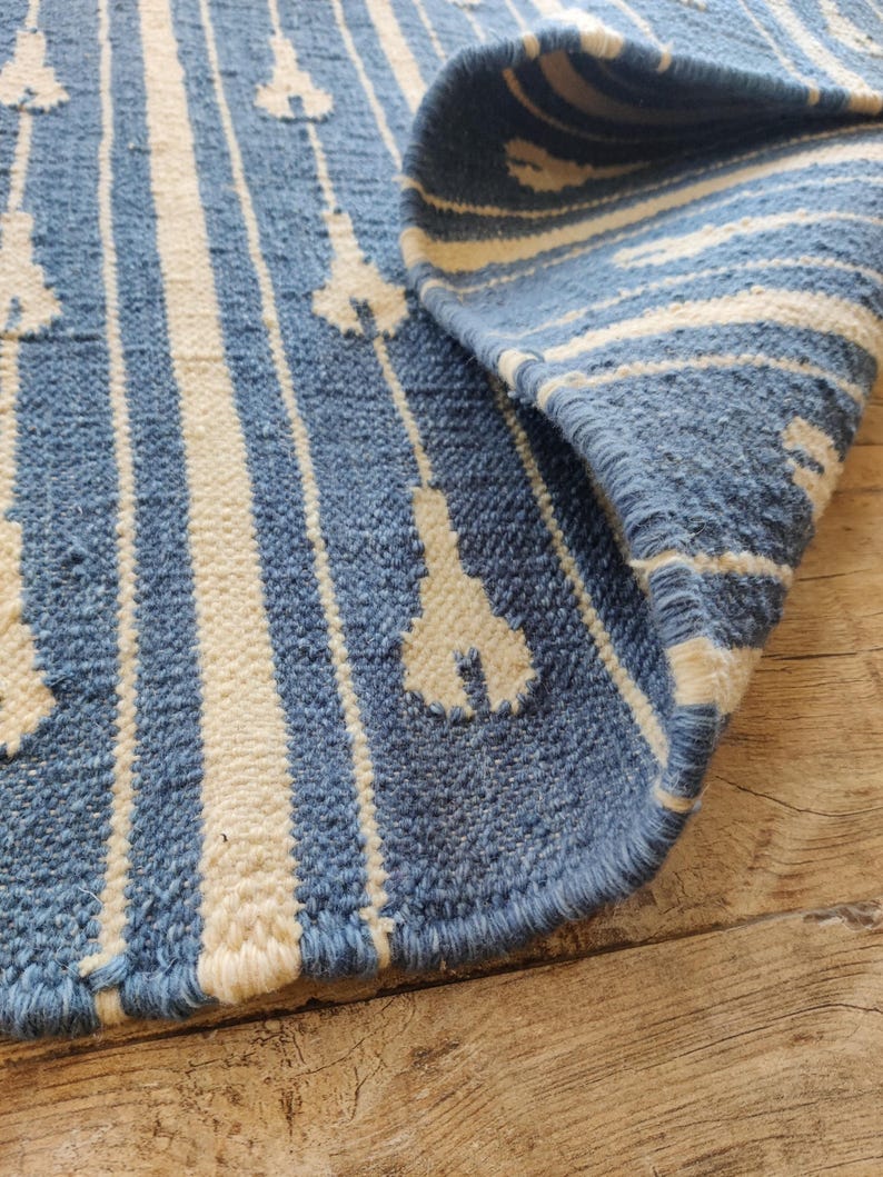 Op de afbeelding: Close-up van een blauw en wit geweven tapijt met een geometrisch patroon. Het tapijt is over zichzelf gevouwen, waardoor de rand van het tapijt zichtbaar is.