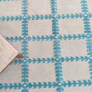Peut inclure: Un tapis blanc avec un motif géométrique bleu. Le motif est composé de carrés avec une bordure bleue et un motif de flèche bleue au centre de chaque carré.