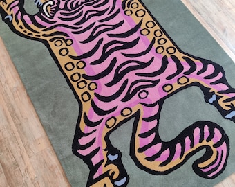 May include: A pink and yellow tiger rug with black stripes on a green background. The tiger is lying on its back with its paws in the air.