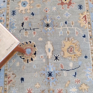 Peut inclure: Un tapis bleu clair avec un motif géométrique dans des tons de bleu, marron et beige. Le motif présente des étoiles, des cercles et d'autres formes abstraites.