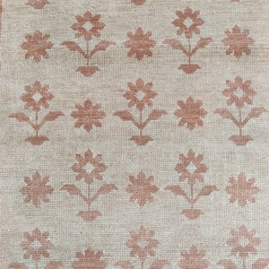 Puede incluir: Una alfombra beige con un patrón repetitivo de flores estilizadas marrones.