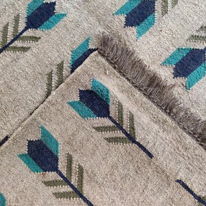 May include: A beige rug with a repeating pattern of teal, dark blue, and green arrows. The rug has a fringe border.