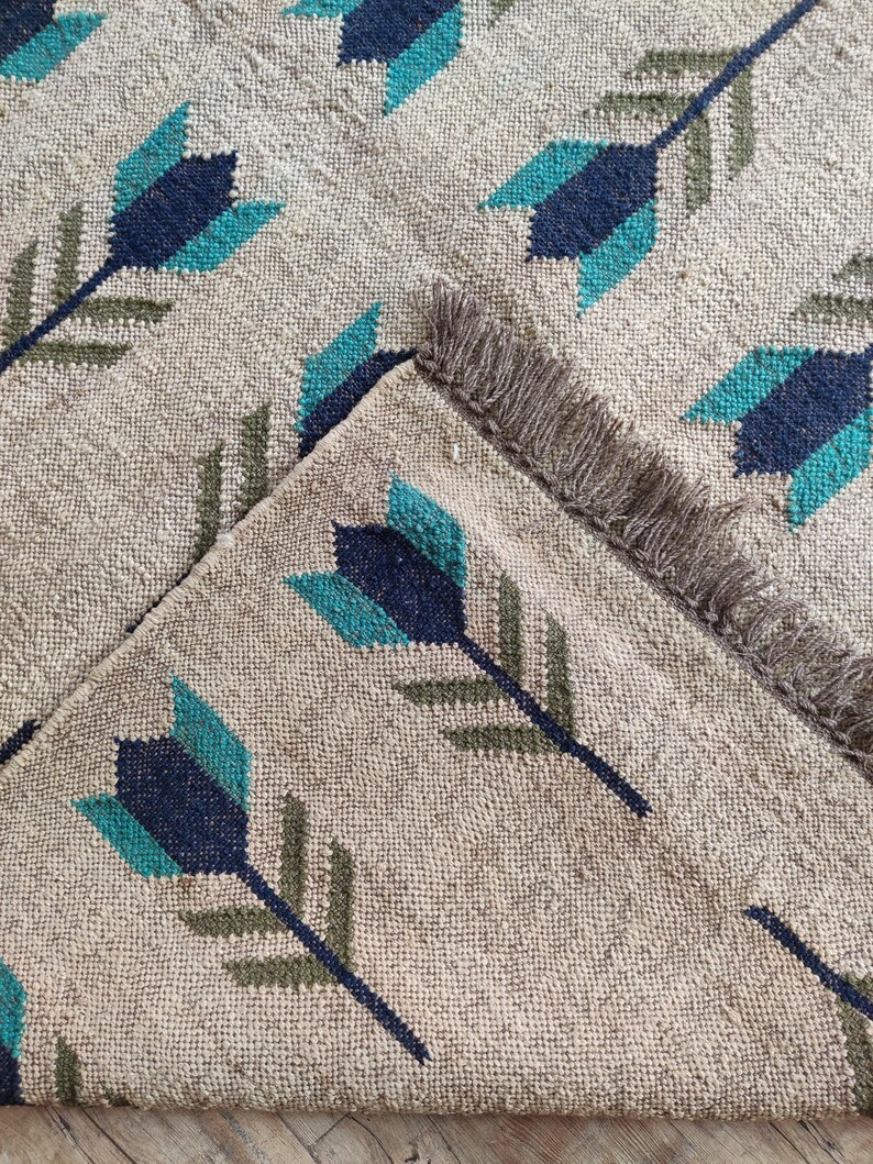 May include: A beige rug with a repeating pattern of teal, dark blue, and green arrows. The rug has a fringe border.