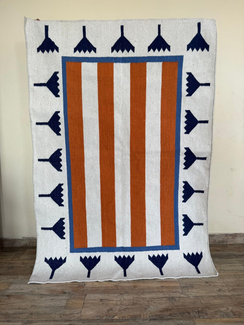 May include: A white rug with a brown and blue geometric pattern. The rug has a border of blue and white flowers.