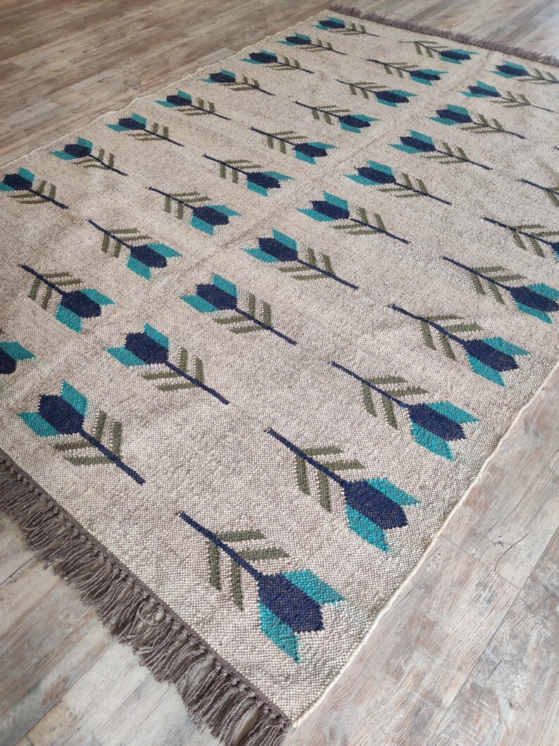 May include: A beige rug with a repeating pattern of teal and dark blue arrows. The rug has a fringe border.