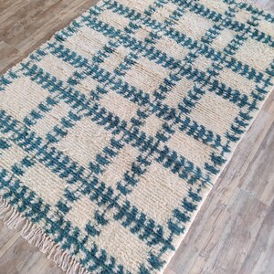 May include: A white and teal blue patterned rug with a fringe border. The rug has a geometric design with a checkered pattern.