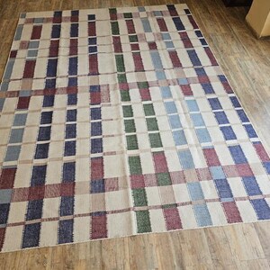 Puede incluir: Una alfombra tejida con un patr&oacute;n de cuadros en tonos de azul, rojo, verde y beige.