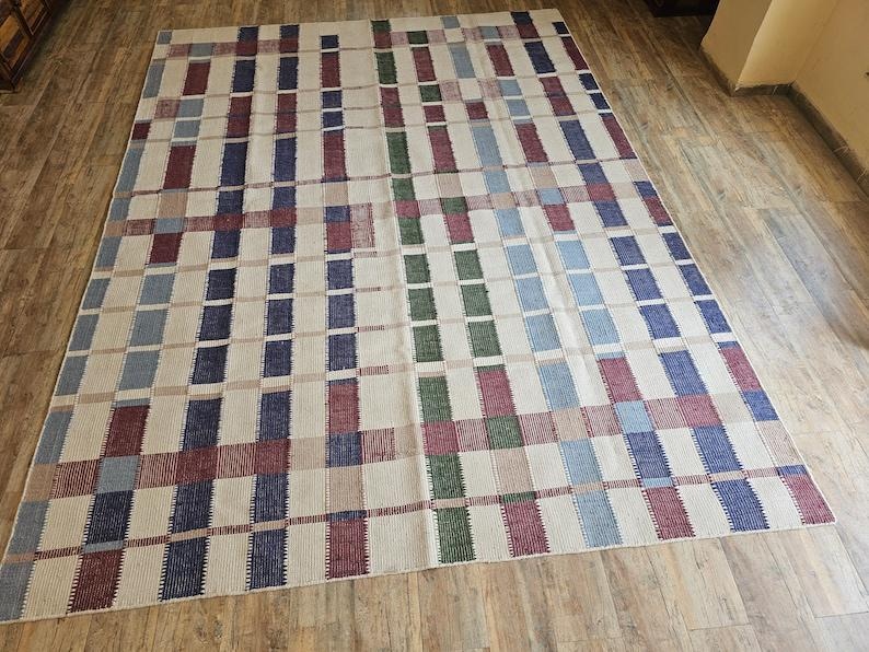 Puede incluir: Una alfombra tejida con un patr&oacute;n de cuadros en tonos de azul, rojo, verde y beige.