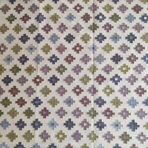 May include: A white rug with a geometric pattern in shades of green, blue, and brown. The pattern is made up of small squares and diamonds.