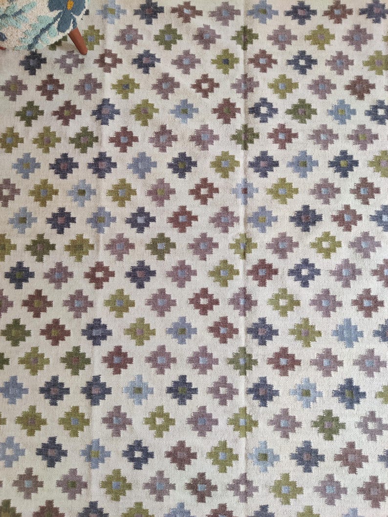 May include: A white rug with a geometric pattern in shades of green, blue, and brown. The pattern is made up of small squares and diamonds.